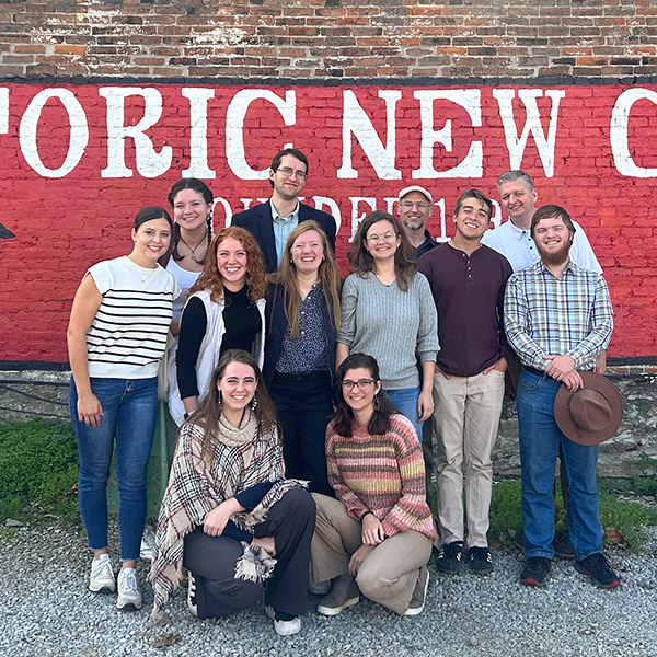 A group of students poses in front of a red brick mural that reads “Historic New Castle” with painted images of a small house and the state of Kentucky.