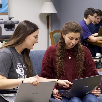Writing Center tutor helping a student with laptops open.