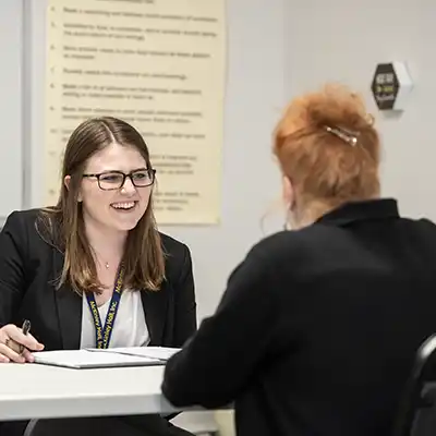 Two females seated at a table discussing an issue, notes are being recorded in a notebook.