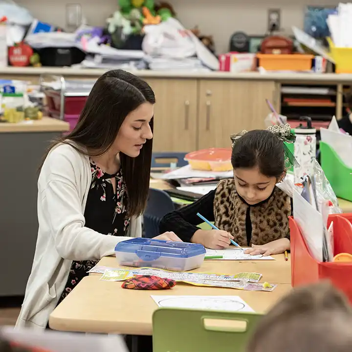 Female teacher educating a young student at a table drawing with colored pencils