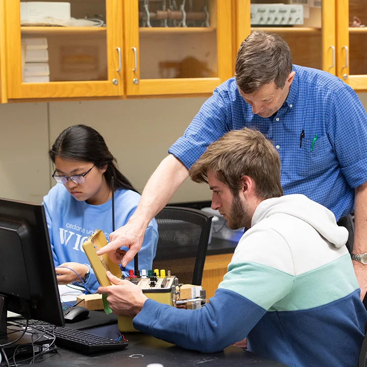 Professor working with students in an electronics lab.