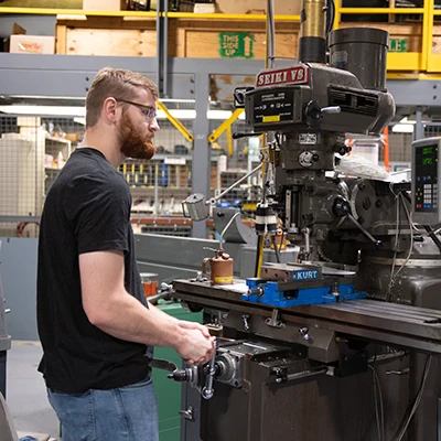 Male student doing metal work using a large milling machine.