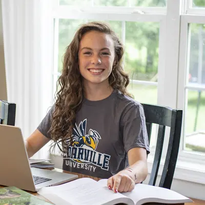 Female student doing homework at a dining room table.