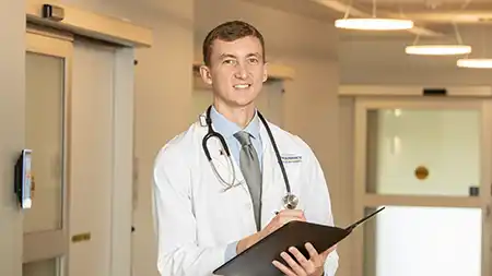 Male phamacy student wearing a stethoscope taking notes.