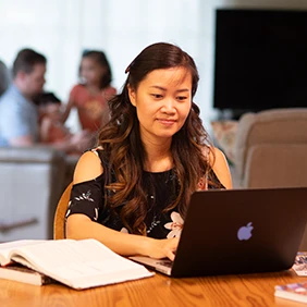 Female high school student sitting at table typing on computer