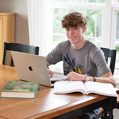 Male high school student smiling while sitting at table with laptop and books.