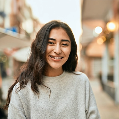 Smiling student wearing a light gray sweatshirt, standing on a softly lit street with blurred buildings in the background.
