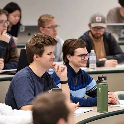 Two male students smiling and listening in classroom.