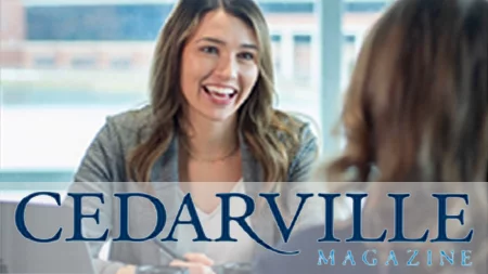 Two women at a desk with a view of Cedar Lake through the window in the background.