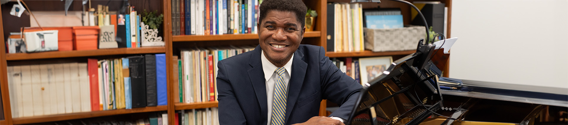 Dr. Lou Lilite sits at the piano in his office with bookshelves in the background.