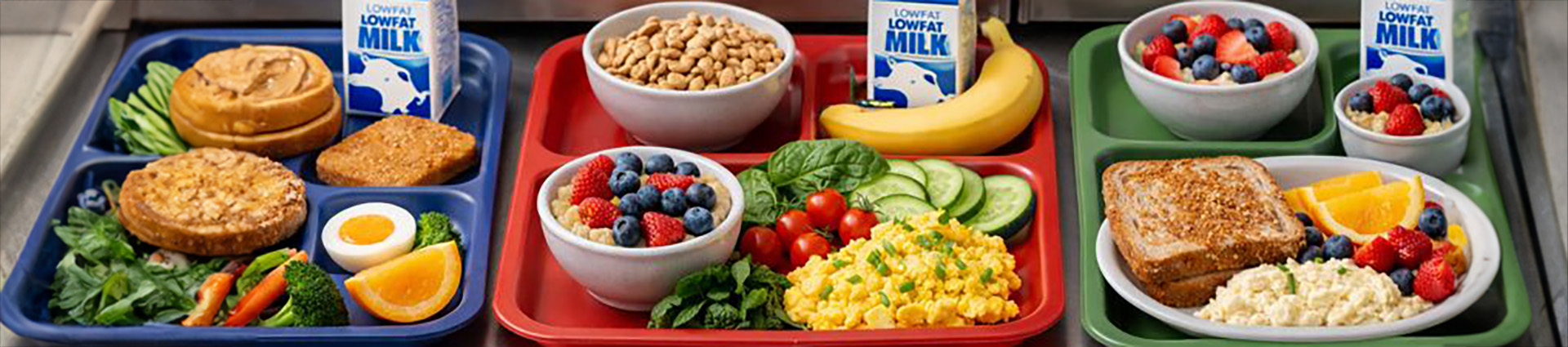 Three school breakfast trays with eggs, breads, vegetables, fruits and milk.