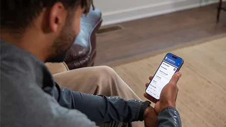 Alumnus views the Cedarville University alumni portal on a smartphone while seated in a living room.