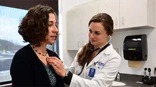 Female nurse using a stethoscope to listening to a female patient's chest.