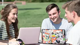 Students studying outside at a table using their laptop computers.