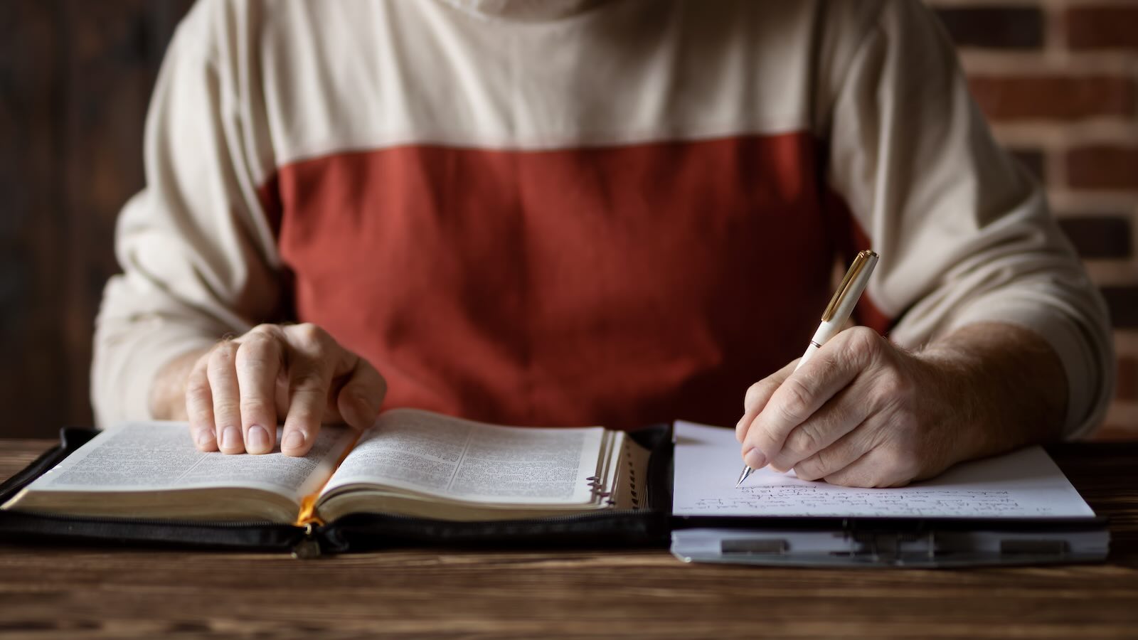 Older man writing notes while referencing Bible.