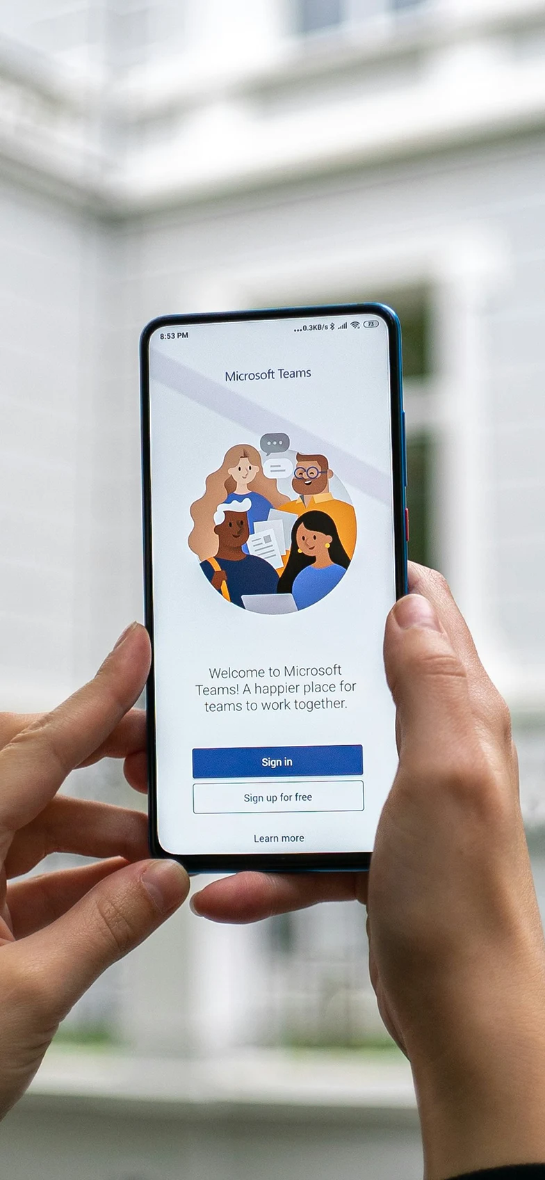 Hands holding a mobile phone displaying Microsoft Teams app login screen.