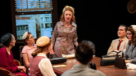 Student actors sitting around a table in a theatre production.